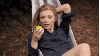 lady swinging in a hammock, eating an apple, with a sly look